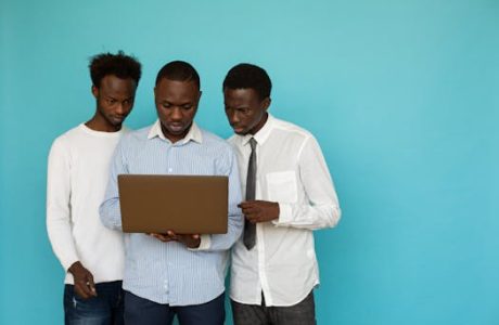 Three men collaborating on a laptop against a teal background, symbolizing teamwork.
